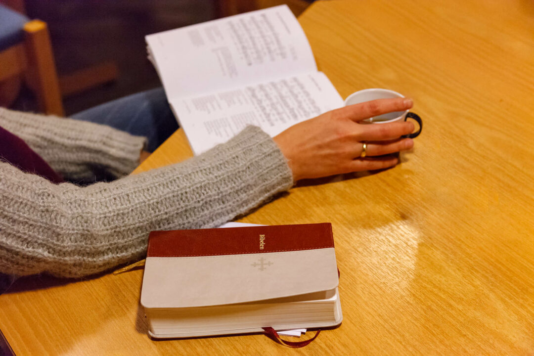 Bilde av et bord med bibel, sangbok og hånd som holder kaffekopp.