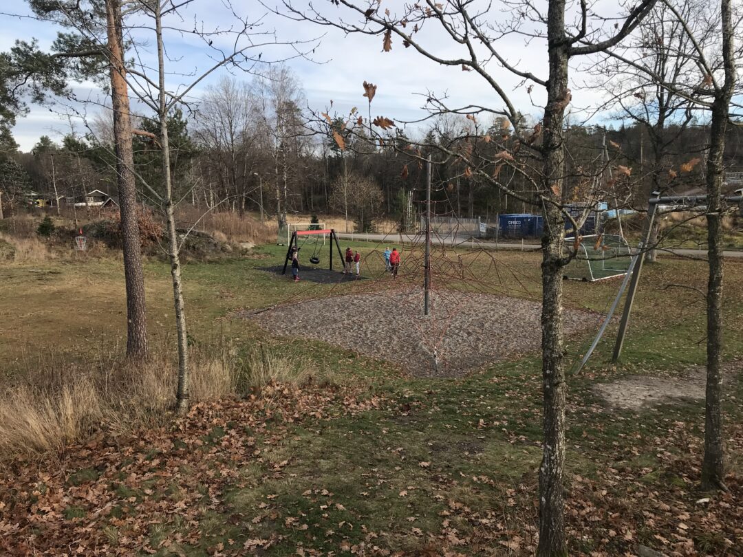 Avstandsbilde av klatretårn og barn ved huskestativ.