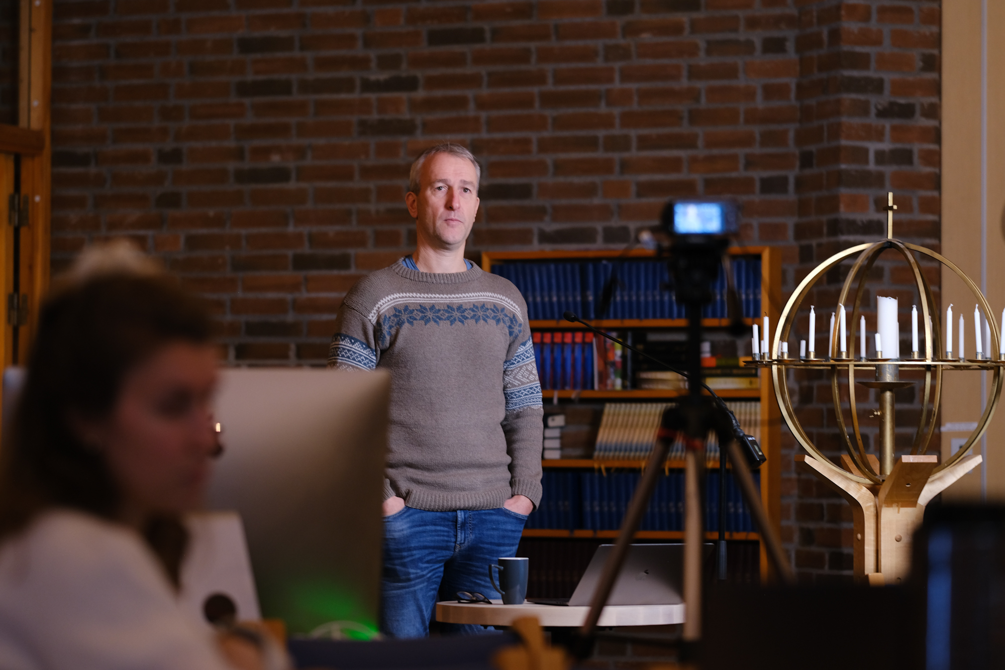 Mann står mellom pc og kamera og snakker