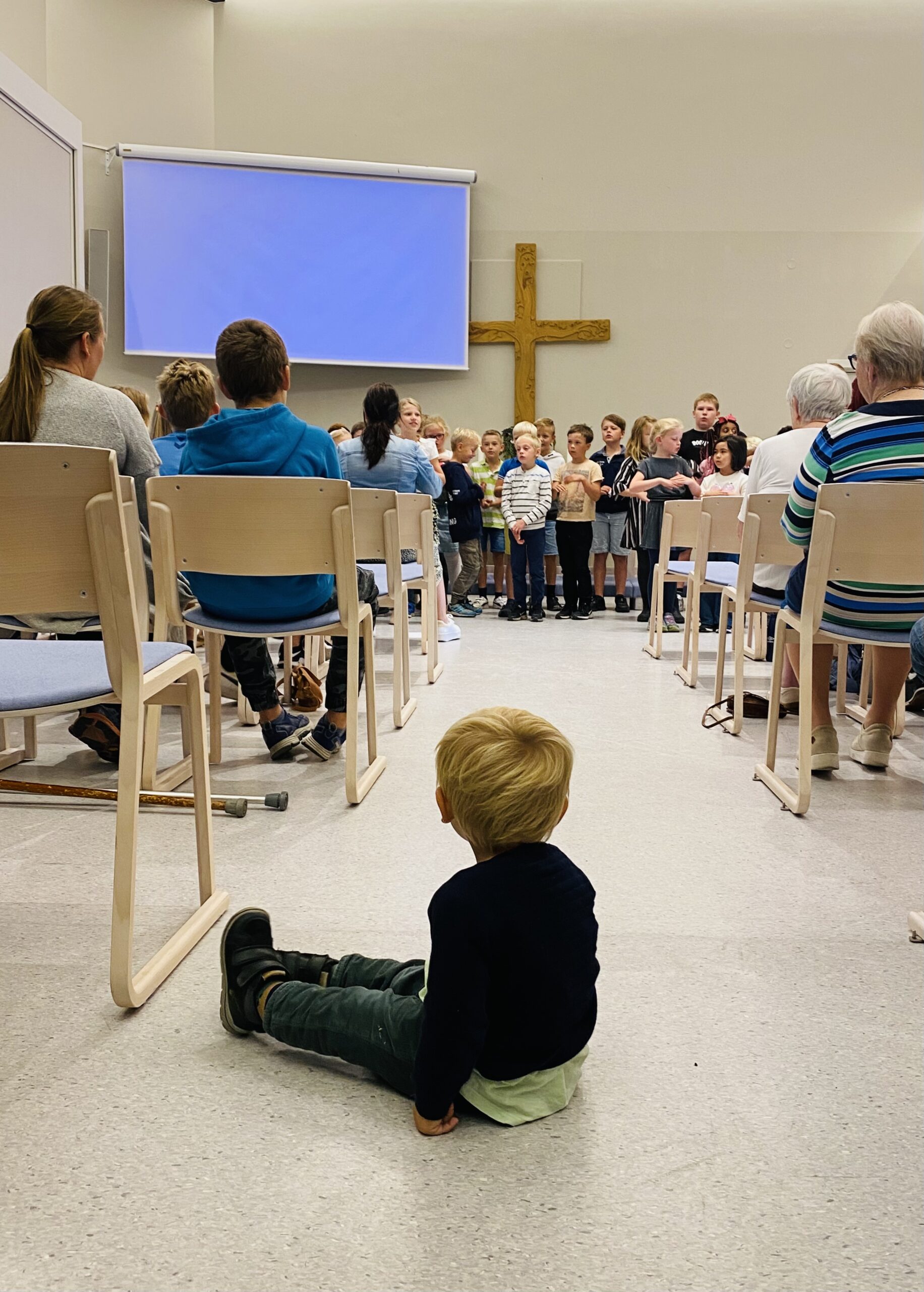 Et lite barn sitter i midtgangen i Moe kirke og ser på småskolekoret som synger.