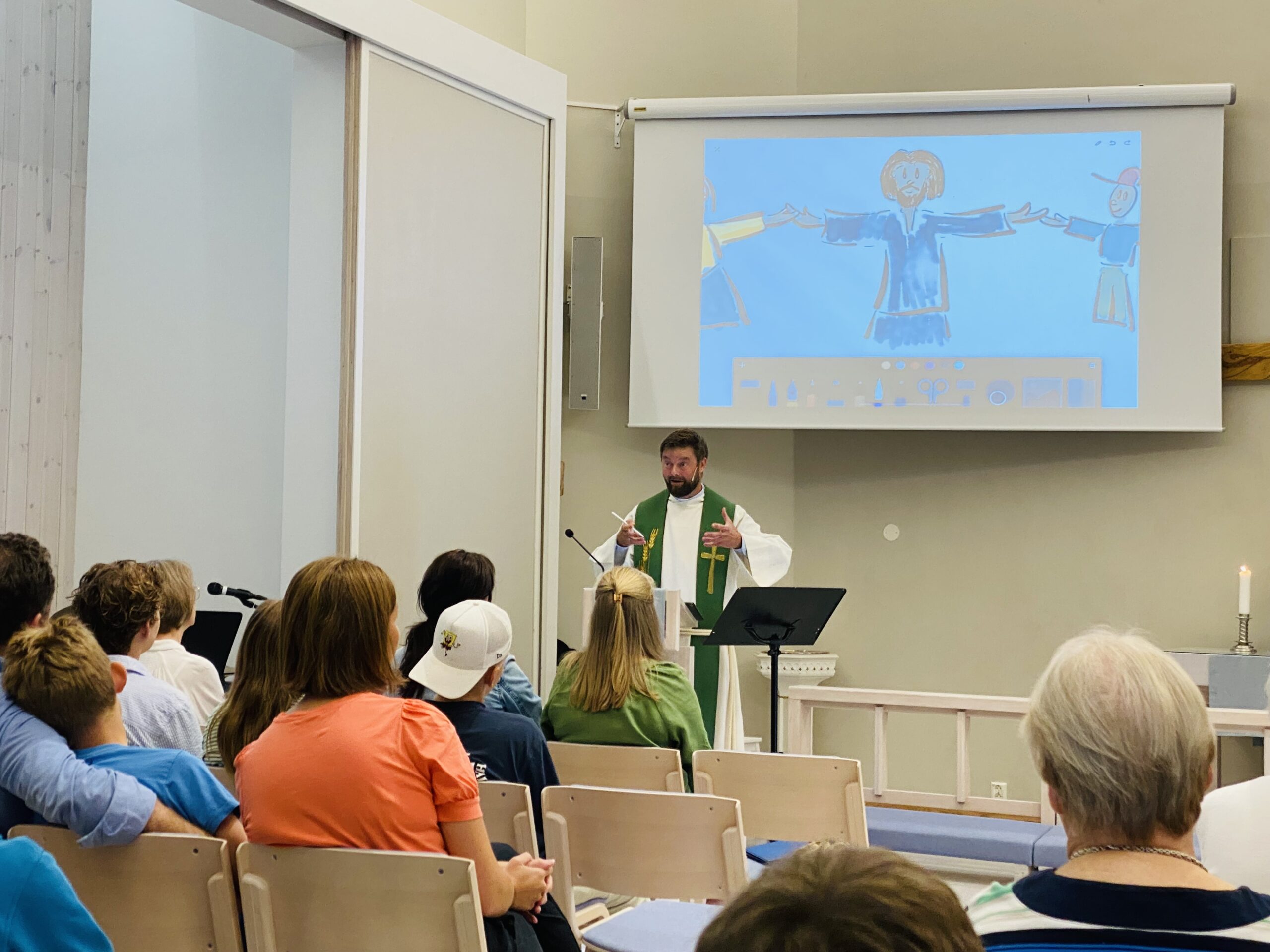 Prest Erling tegner under preken på skolegudstjeneste.