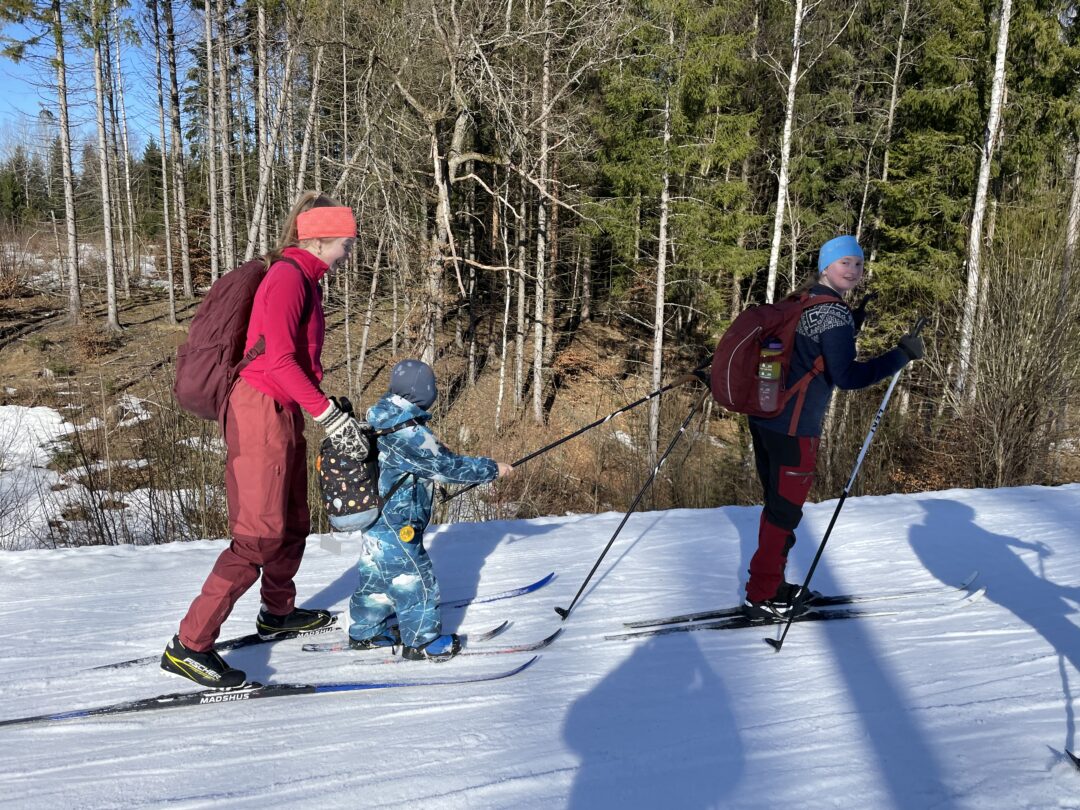 To store jenter hjelper en liten gutt på ski.