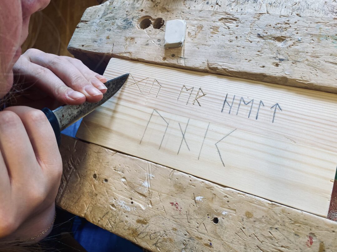 Runer på en trebit risses inn med kniv.