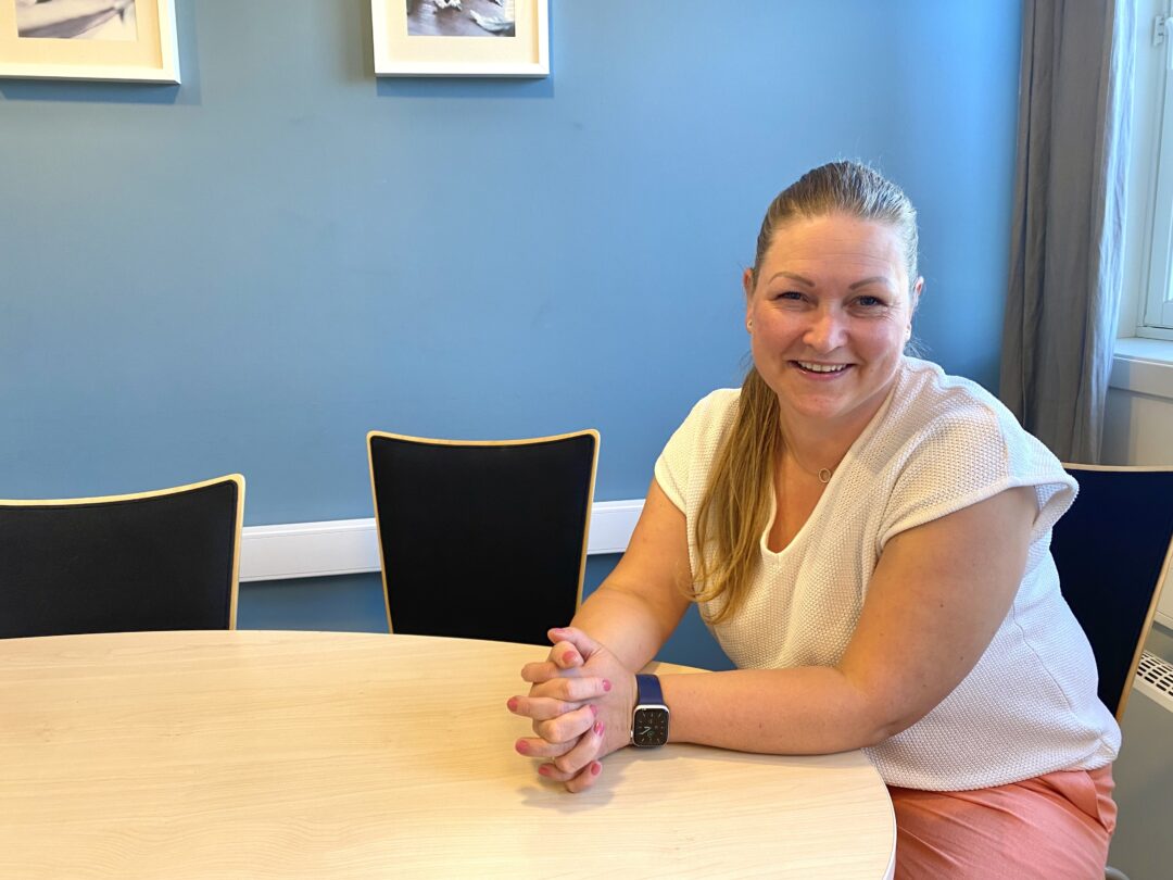 Helsesykepleier, Maria Bjørndal, sitter ved et bord og ønkser velkommen til samtaler.