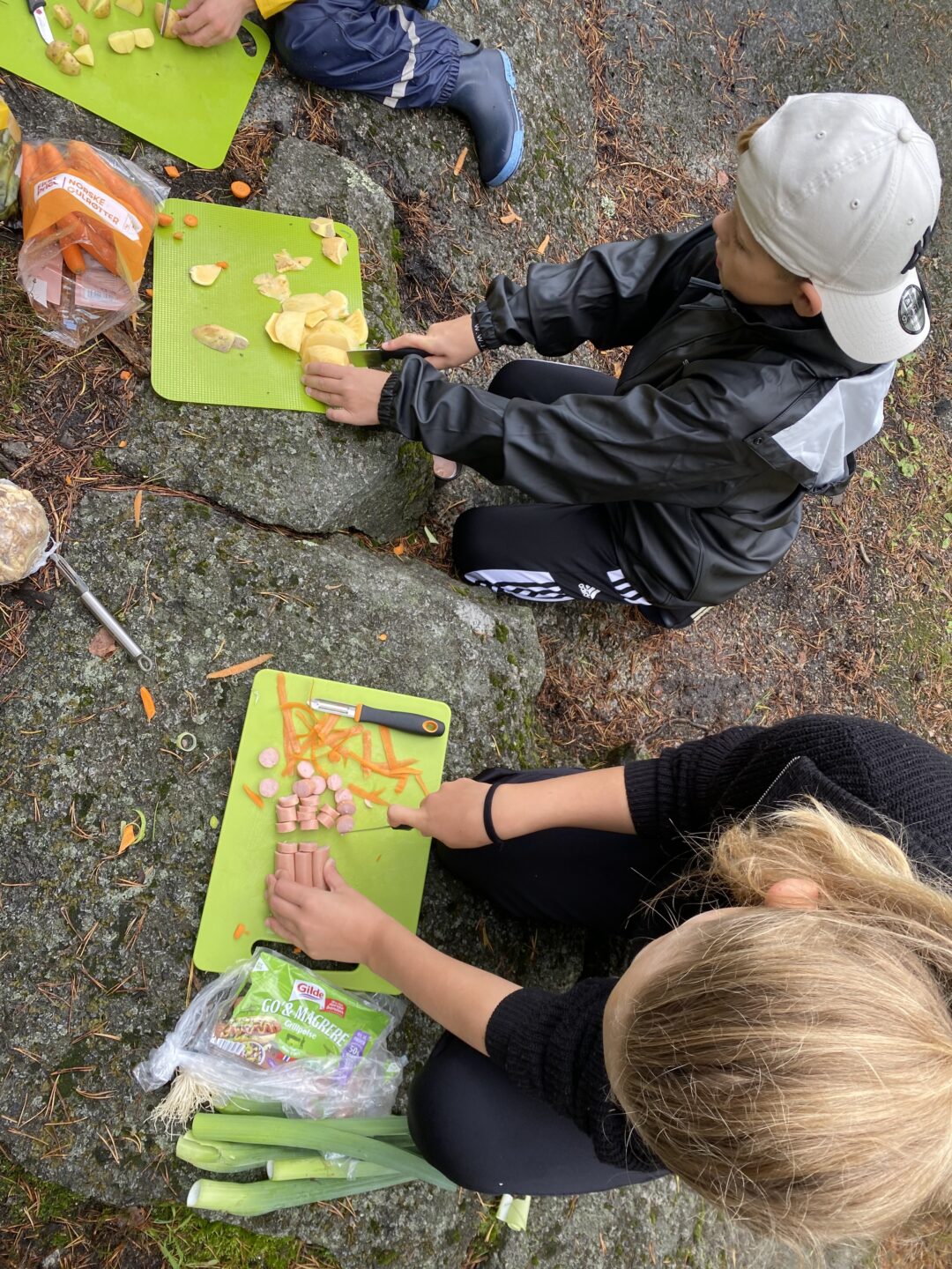 Bilde av tre elever som kutter grønnsaker ute.