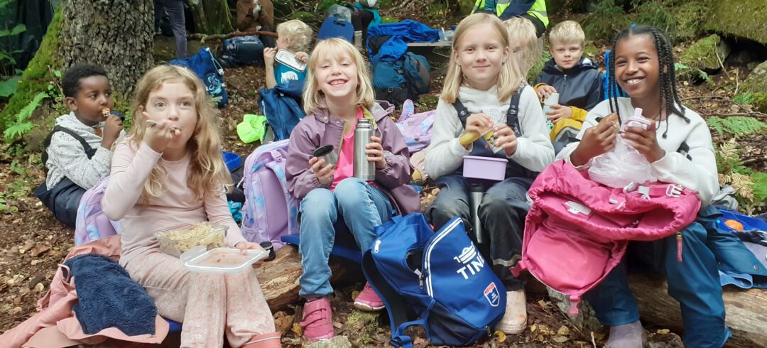 Bilde av mange elever som sitter og spiser i skogen.