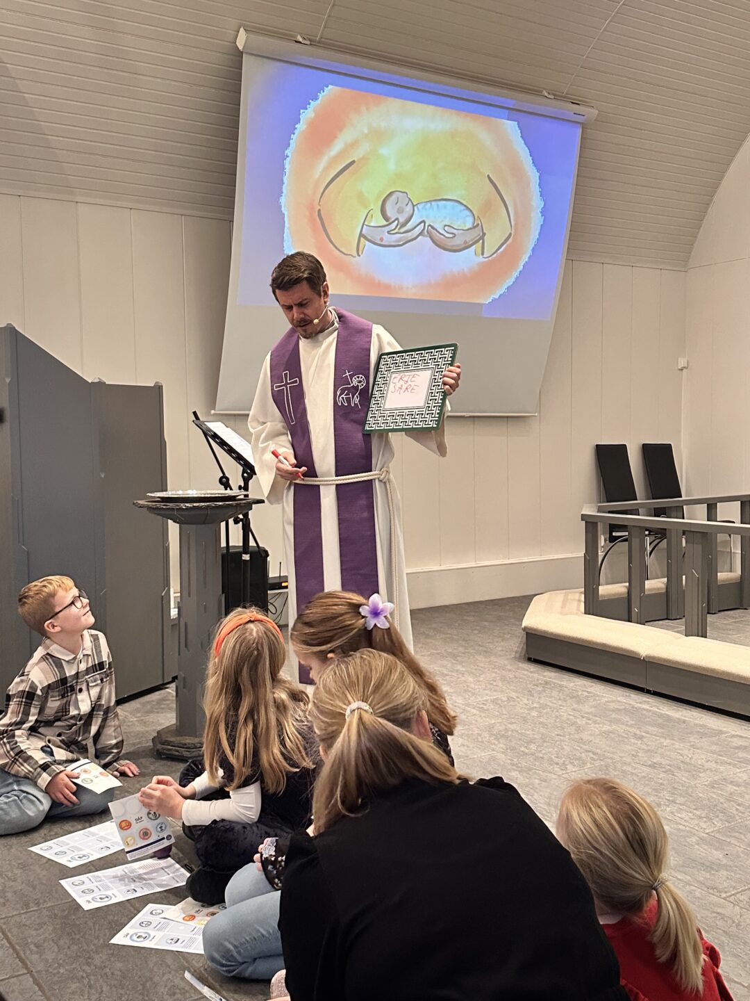 Bilde av Peter prest som forteller til barn på gulvet i kirken.