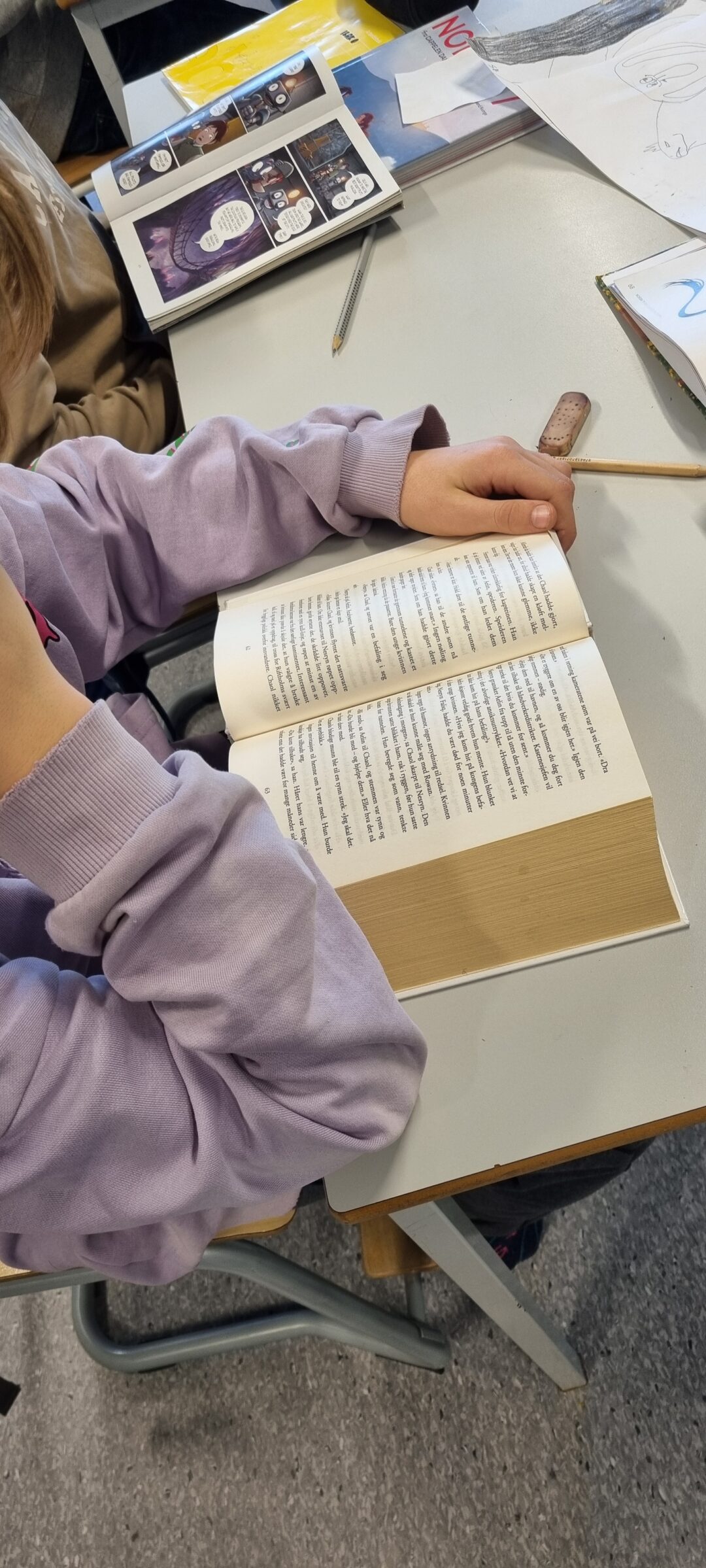 Bilde av elev (skjult) som leser tykk bok med mye tekst.