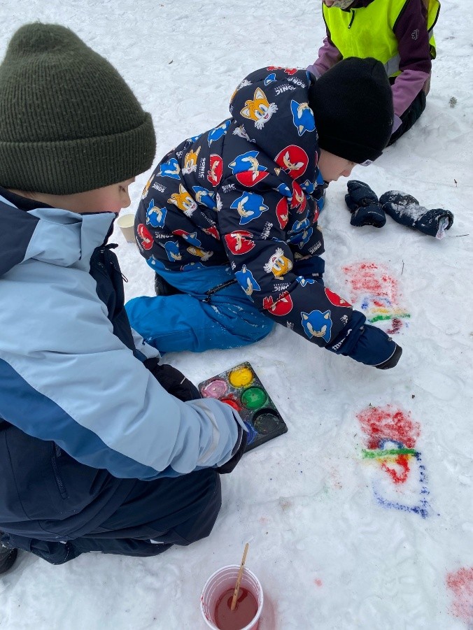 Bilde av elever som maler det samiske flagget i snøen.