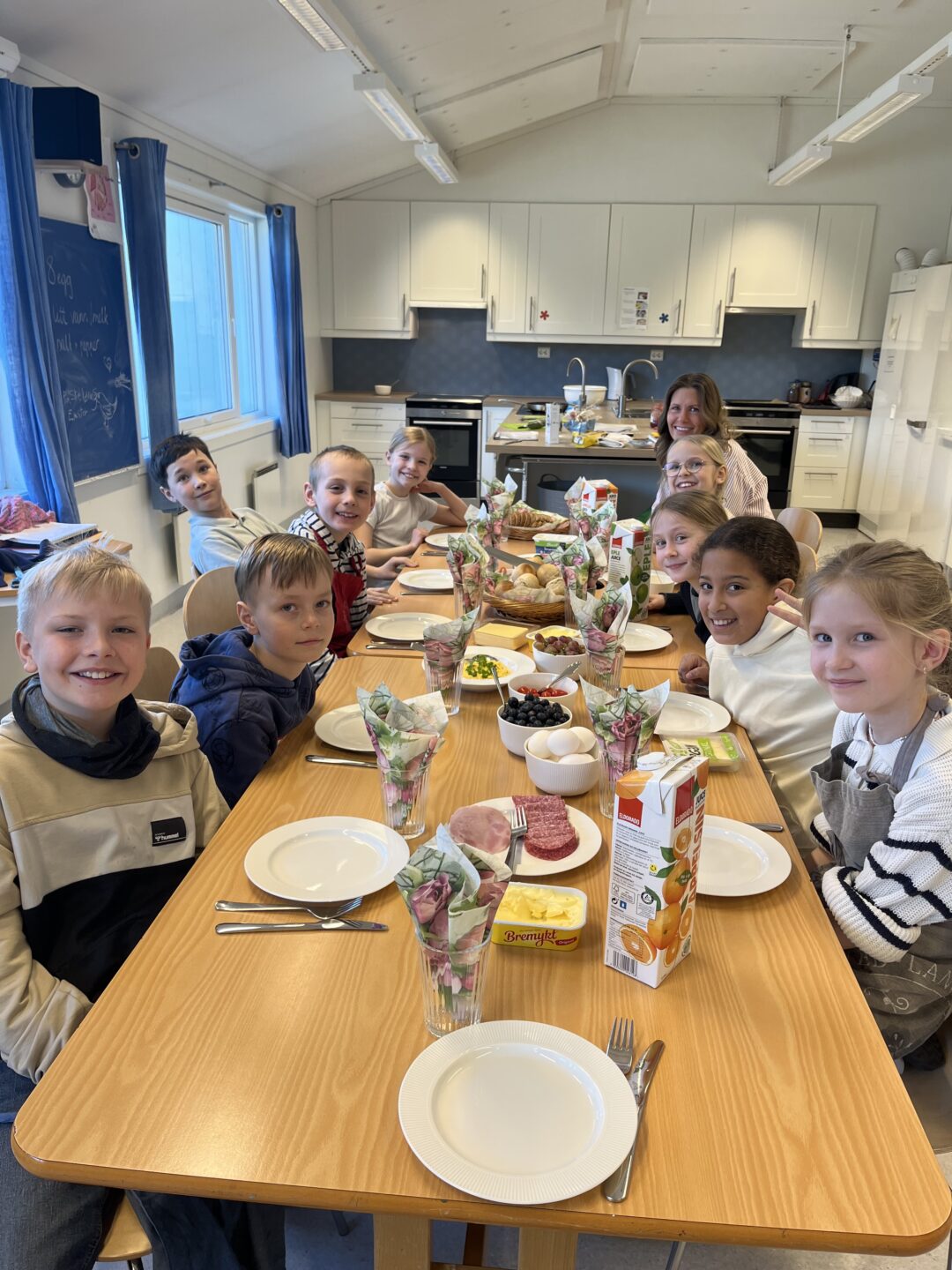 Bilde av elever som sitter rundt et lunsjbord på skolekjøkkenet.