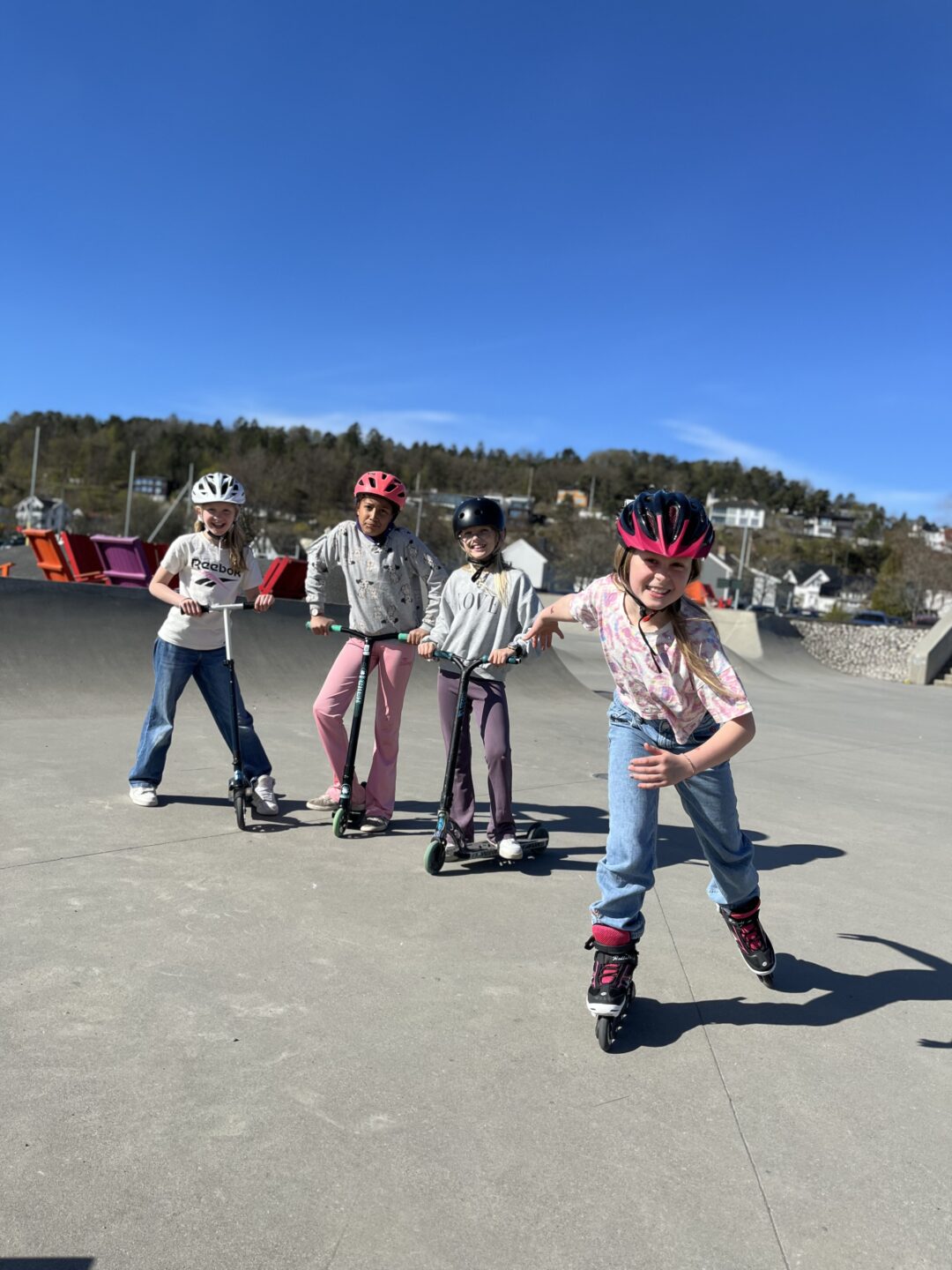 Bilde av fire jenter på rulleskøyter og sparkesykkel i skatepark.