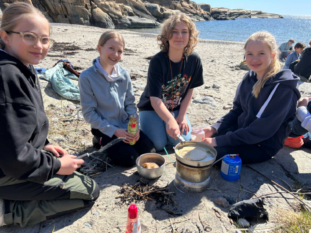 Bilde av fire jenter som steker pannekaker på primus på stranden.