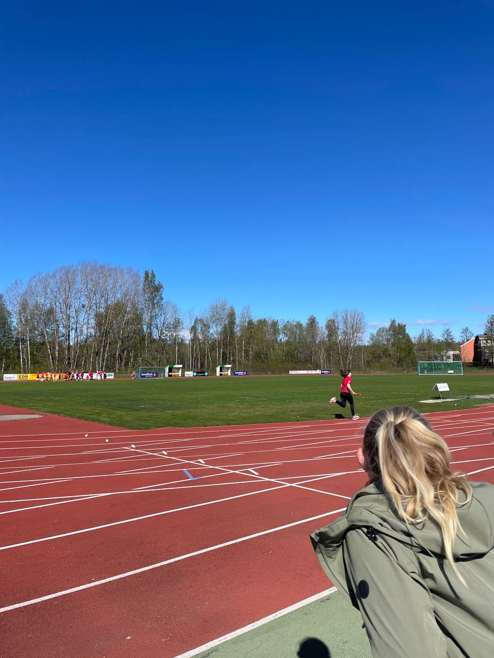 Bilde av en jente bakfra som ser på en jente på avstand som løper på bane.